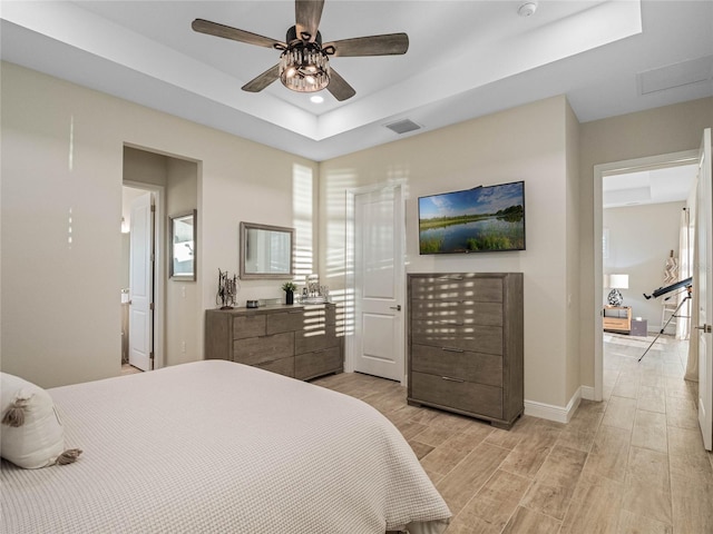 bedroom with ceiling fan, a tray ceiling, and light hardwood / wood-style floors