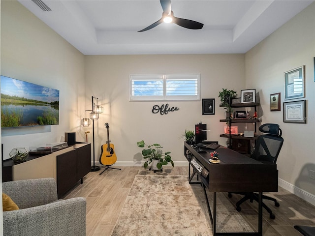 home office featuring light hardwood / wood-style floors, a raised ceiling, and ceiling fan