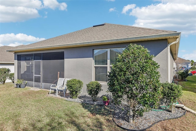 back of property with a shingled roof, a lawn, a sunroom, and stucco siding