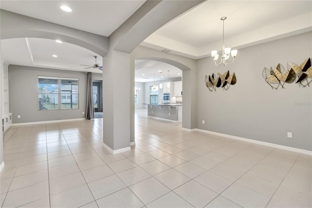 empty room with a tray ceiling, arched walkways, and light tile patterned floors