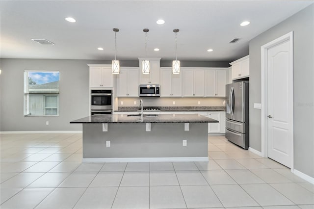 kitchen featuring visible vents, dark stone counters, appliances with stainless steel finishes, a breakfast bar, and a sink