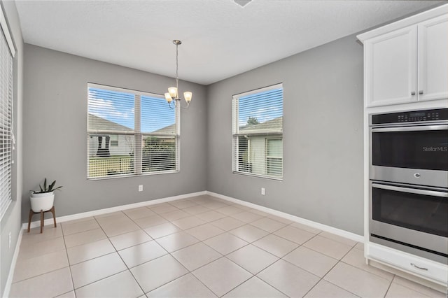 unfurnished dining area with light tile patterned flooring, a notable chandelier, a textured ceiling, and baseboards