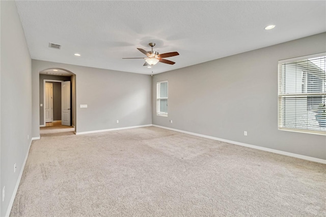 spare room with arched walkways, light carpet, a ceiling fan, and baseboards