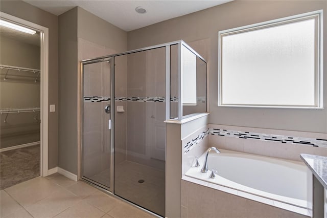 full bath with a garden tub, a shower stall, a walk in closet, and tile patterned flooring