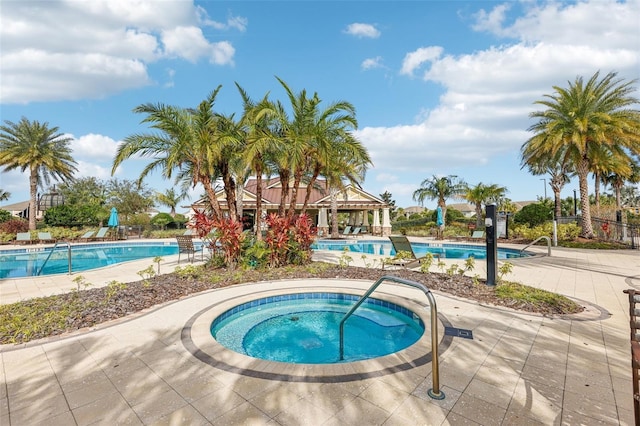 community pool with a patio area, fence, and a hot tub