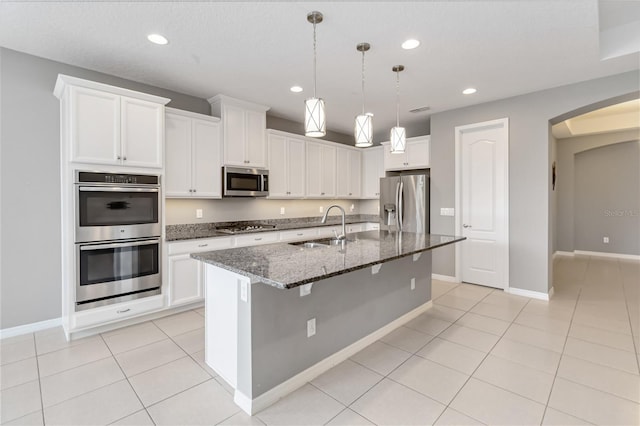 kitchen with arched walkways, light tile patterned flooring, stainless steel appliances, a sink, and dark stone countertops