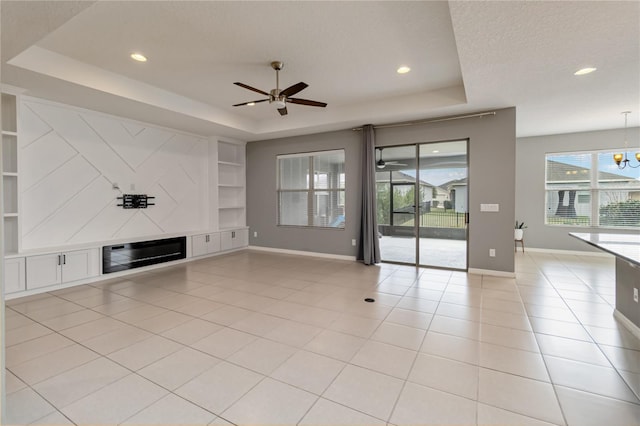 unfurnished living room featuring built in features, light tile patterned floors, a raised ceiling, a textured ceiling, and baseboards