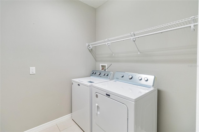 clothes washing area featuring laundry area, separate washer and dryer, light tile patterned flooring, and baseboards