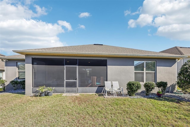 back of property featuring a sunroom, a shingled roof, a lawn, and stucco siding