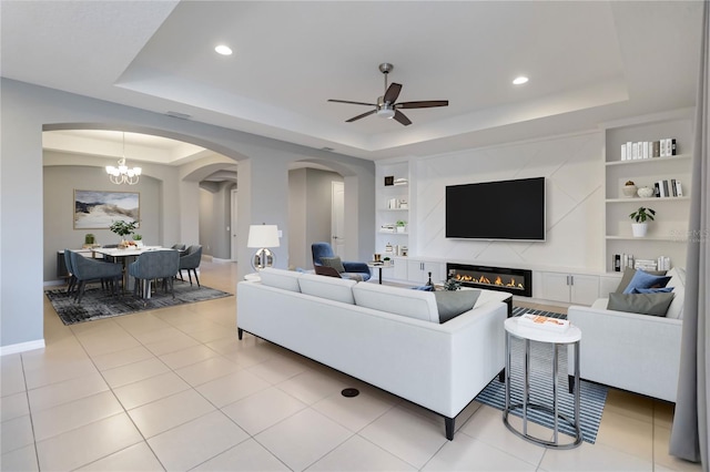 living area featuring built in features, a raised ceiling, a fireplace, and light tile patterned floors