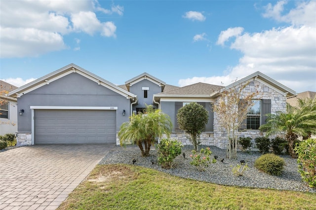 ranch-style house featuring decorative driveway, stone siding, an attached garage, and stucco siding