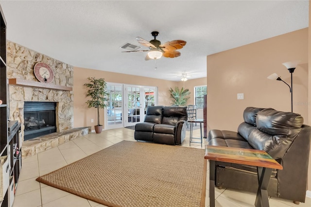 living room featuring french doors, ceiling fan, light tile patterned flooring, and a stone fireplace