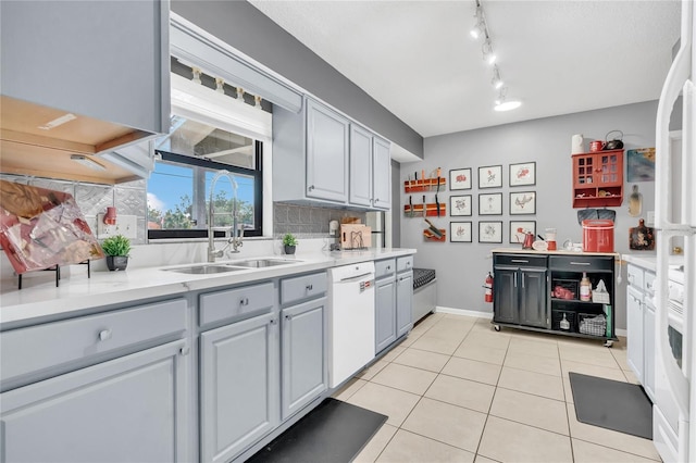 kitchen featuring white appliances, light tile patterned floors, decorative backsplash, gray cabinets, and sink