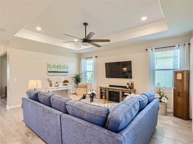 living room with ornamental molding, ceiling fan, light hardwood / wood-style floors, and a tray ceiling