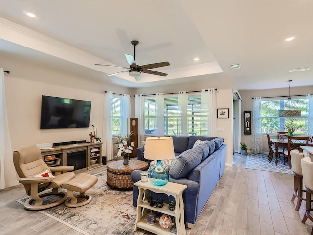 living room featuring a raised ceiling, ceiling fan, crown molding, and light wood-type flooring