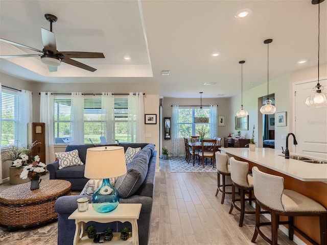 living room with ceiling fan, light hardwood / wood-style floors, a raised ceiling, and sink