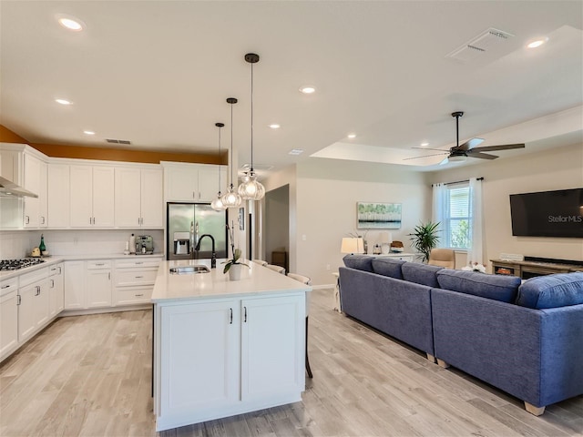 kitchen featuring appliances with stainless steel finishes, decorative light fixtures, an island with sink, sink, and white cabinets