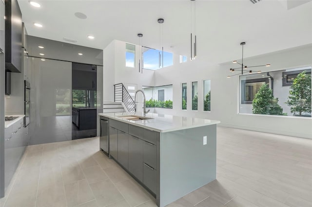 kitchen featuring a center island with sink, stainless steel dishwasher, sink, and hanging light fixtures