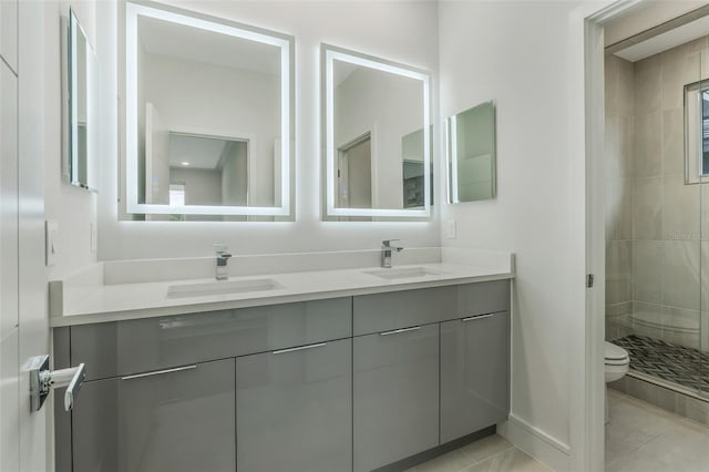 bathroom with tile patterned flooring, a tile shower, vanity, and toilet