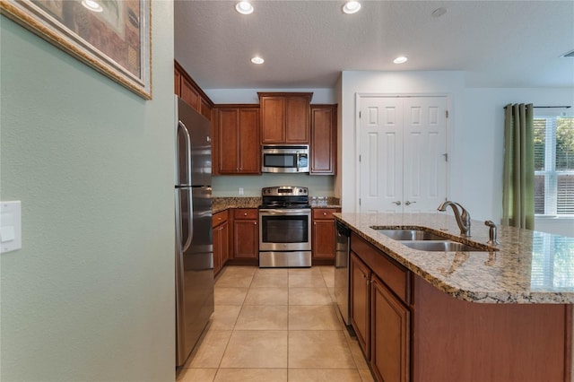 kitchen with light stone countertops, appliances with stainless steel finishes, sink, light tile patterned floors, and a center island with sink