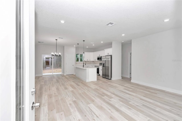 kitchen featuring appliances with stainless steel finishes, decorative light fixtures, a center island with sink, white cabinets, and a chandelier