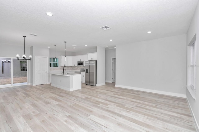 kitchen with white cabinetry, hanging light fixtures, stainless steel appliances, a chandelier, and a kitchen island with sink