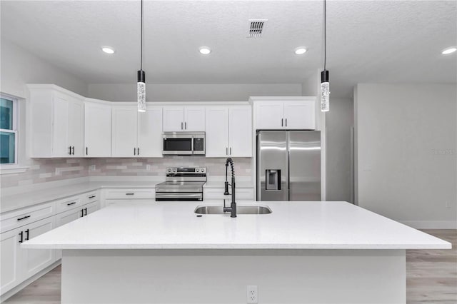 kitchen featuring appliances with stainless steel finishes, a kitchen island with sink, sink, decorative light fixtures, and white cabinetry