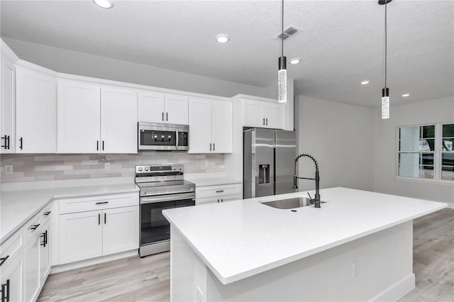 kitchen featuring appliances with stainless steel finishes, sink, pendant lighting, a center island with sink, and white cabinets