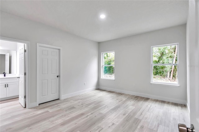 unfurnished bedroom featuring connected bathroom, light hardwood / wood-style flooring, and multiple windows