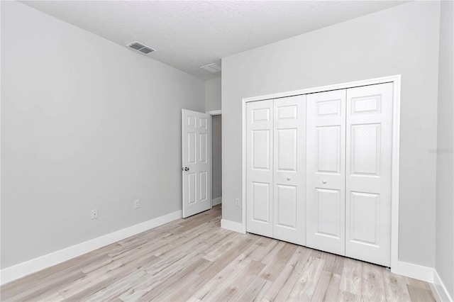 unfurnished bedroom with a textured ceiling, light wood-type flooring, and a closet