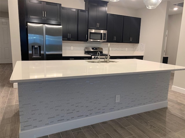 kitchen featuring an island with sink, appliances with stainless steel finishes, decorative backsplash, and sink