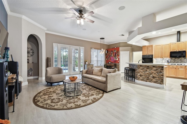 living room featuring sink, light wood-type flooring, crown molding, and ceiling fan with notable chandelier