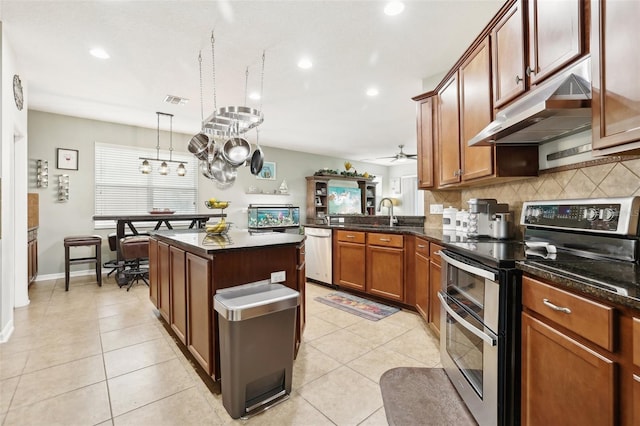 kitchen featuring kitchen peninsula, dark stone counters, stainless steel appliances, ceiling fan, and hanging light fixtures