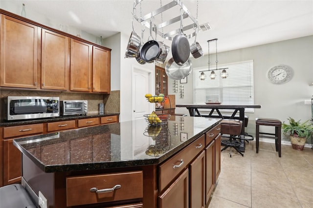 kitchen featuring decorative backsplash, dark stone counters, a kitchen island, hanging light fixtures, and light tile patterned flooring