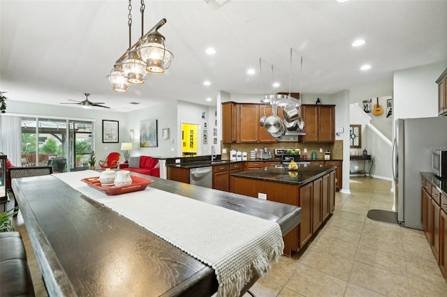 kitchen featuring kitchen peninsula, appliances with stainless steel finishes, ceiling fan with notable chandelier, sink, and pendant lighting