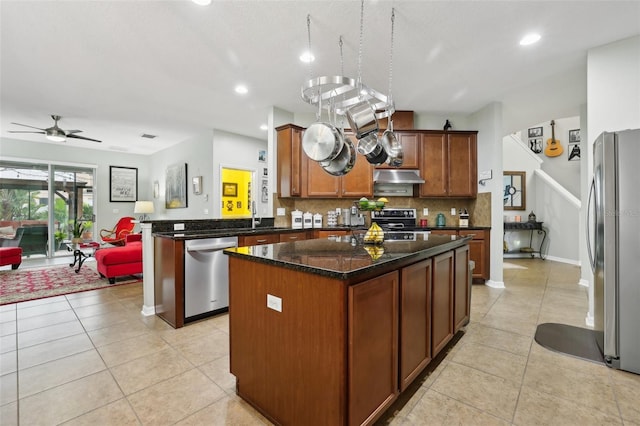 kitchen with stainless steel appliances, light tile patterned floors, kitchen peninsula, dark stone countertops, and a kitchen island