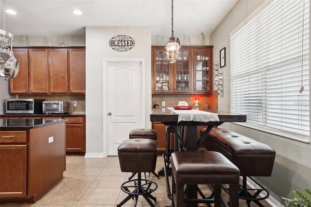 kitchen featuring backsplash, light tile patterned floors, pendant lighting, dark stone countertops, and a breakfast bar area