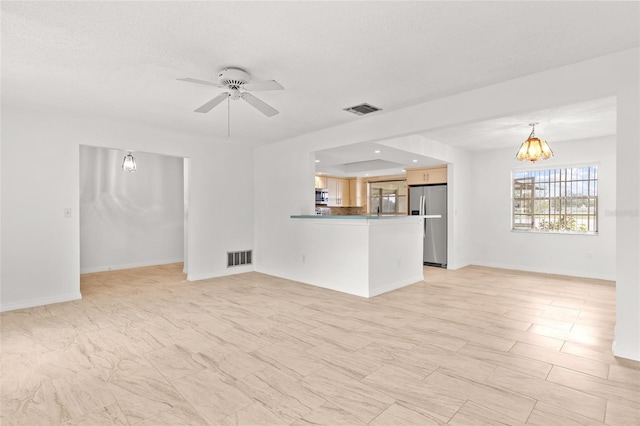 unfurnished living room featuring baseboards, visible vents, and ceiling fan with notable chandelier