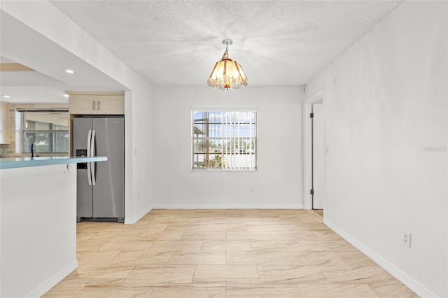 unfurnished dining area featuring recessed lighting, a textured ceiling, baseboards, and an inviting chandelier