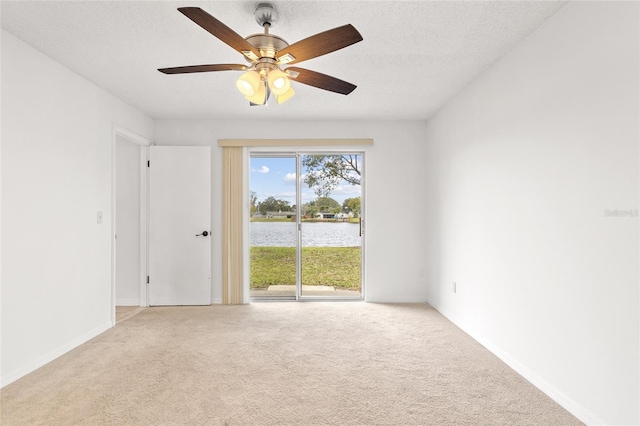 unfurnished room with carpet floors, a water view, a textured ceiling, and baseboards