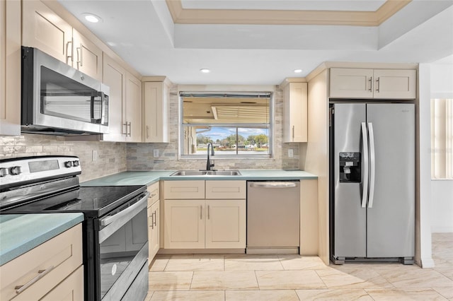 kitchen featuring cream cabinets, a tray ceiling, stainless steel appliances, light countertops, and a sink