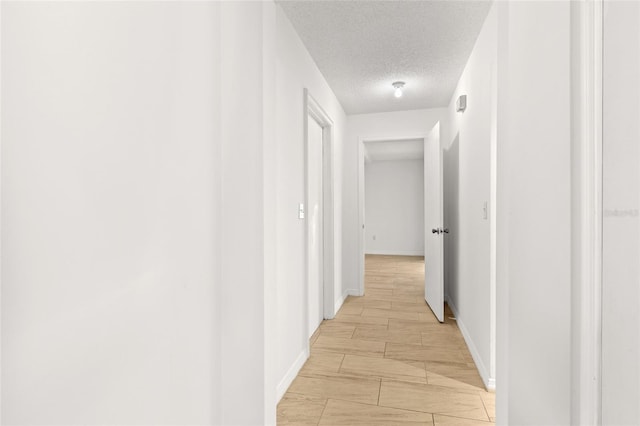 corridor with a textured ceiling and baseboards