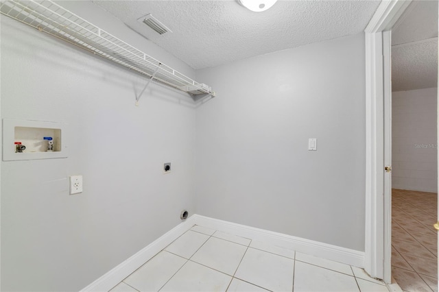 clothes washing area with hookup for an electric dryer, light tile patterned floors, a textured ceiling, and hookup for a washing machine