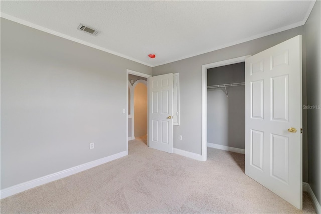 unfurnished bedroom featuring a closet, light colored carpet, a textured ceiling, and ornamental molding