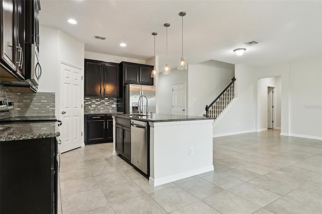 kitchen with pendant lighting, backsplash, dark stone counters, an island with sink, and stainless steel appliances