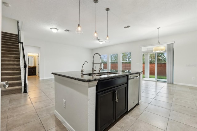 kitchen featuring dark stone countertops, dishwasher, sink, and an island with sink