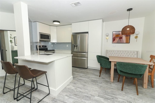 kitchen featuring pendant lighting, white cabinetry, light hardwood / wood-style floors, kitchen peninsula, and stainless steel appliances