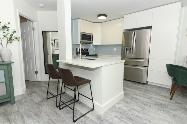 kitchen featuring tasteful backsplash, stainless steel appliances, sink, light hardwood / wood-style flooring, and white cabinetry