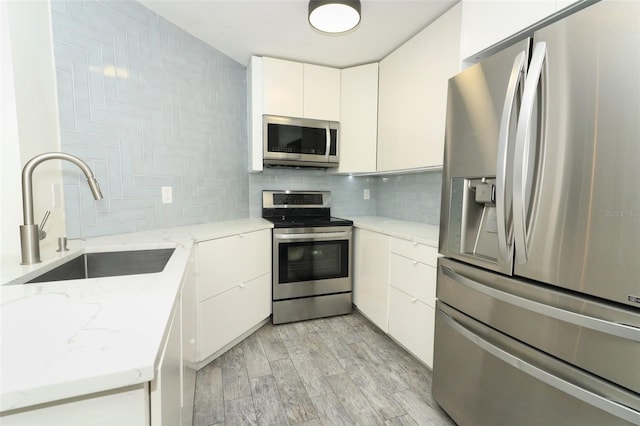 kitchen featuring sink, decorative backsplash, light wood-type flooring, appliances with stainless steel finishes, and white cabinetry