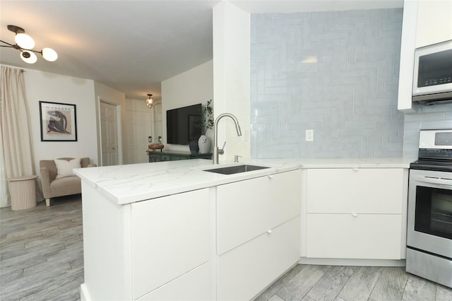 kitchen featuring kitchen peninsula, light stone countertops, white cabinets, and stainless steel range oven